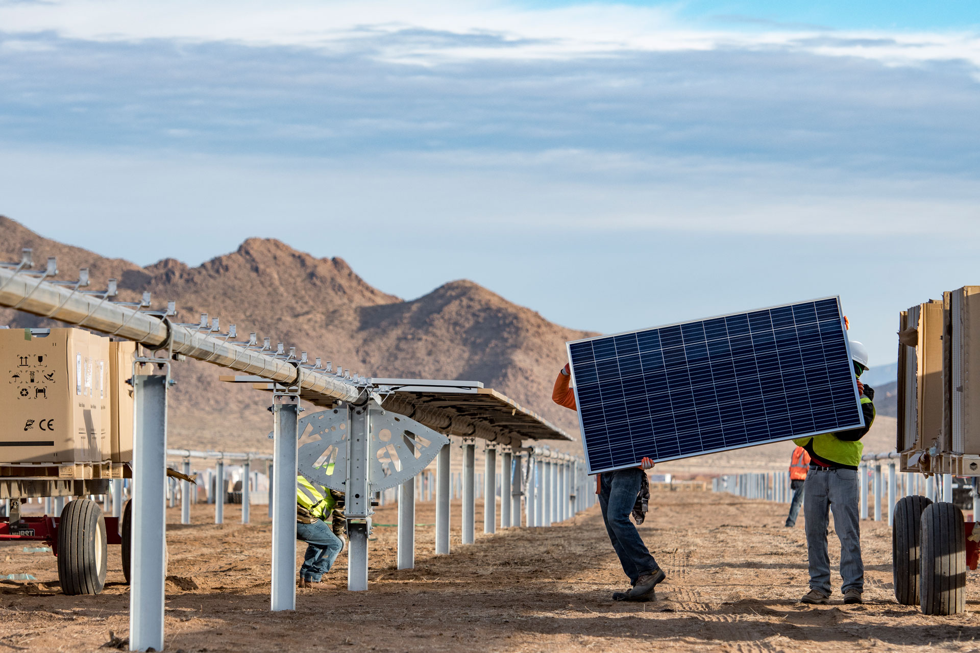 Construction workers lifting a solar panel at Gray Hawk solar, set against the desert and mountains of Arizona. 
